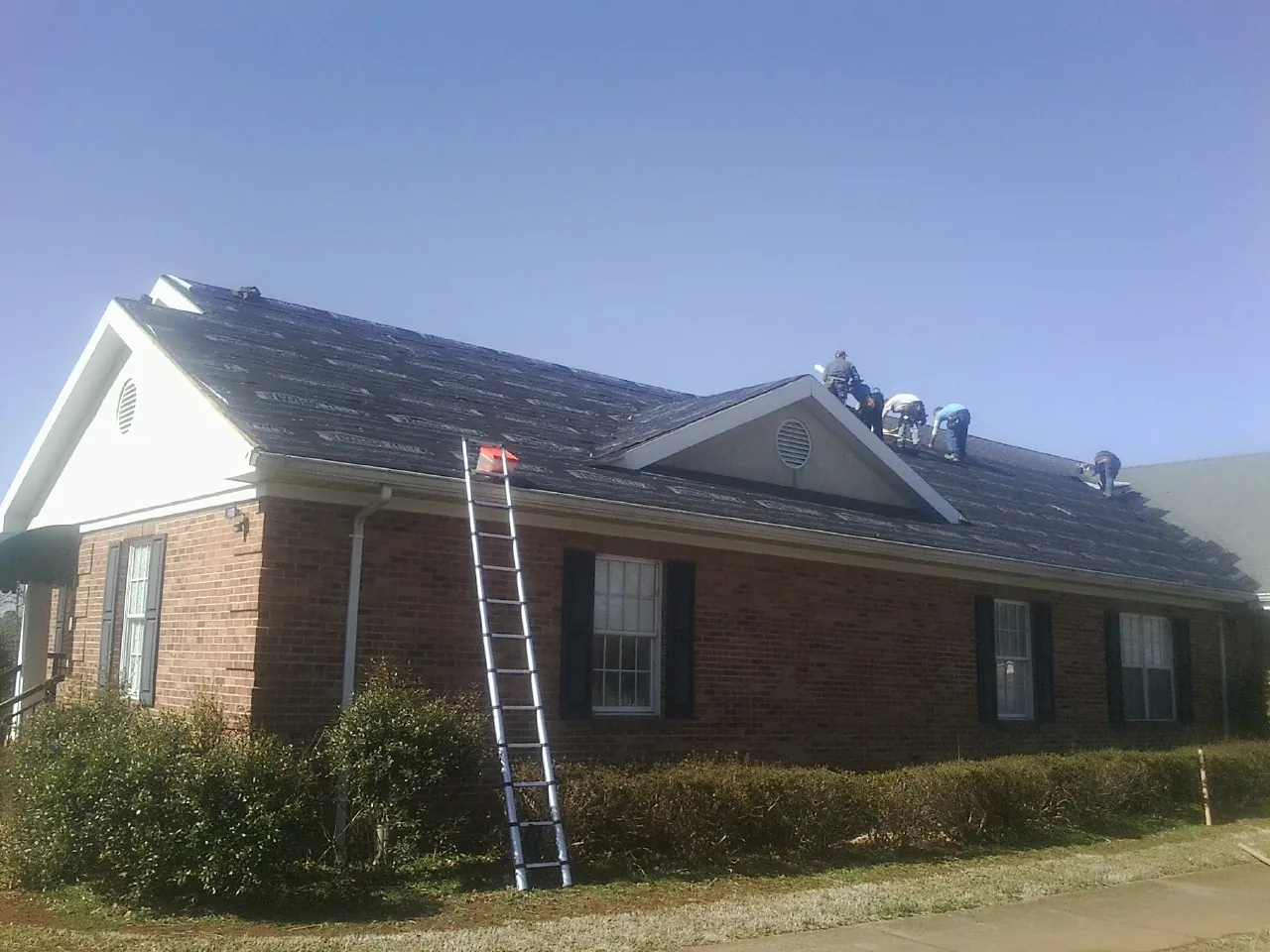 Crew tearing shingles off a brick ranch roof with a ladder set — Metal Roof Repair work by our crew in Paris